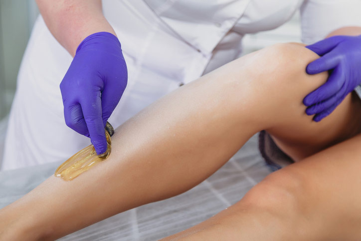 Beautician wearing purple latex gloves applies sugaring solution to a woman's leg at The Facial Center in Charleston, WV