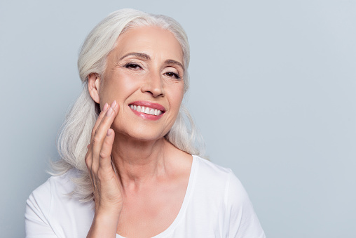 A smiling woman touching her face after facelift procedure from The Facial Center in Charleston, WV