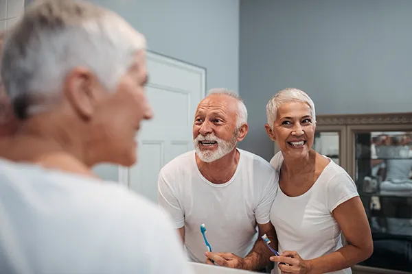 Elderly couple smiling and brushing their teeth in the bathroom mirror