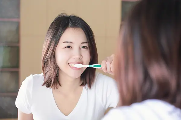 Young woman brushing her teeth in front of a bathroom mirror, focused on good dental care practices.