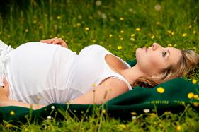 Pregnant woman laying down in grass looking at the sky